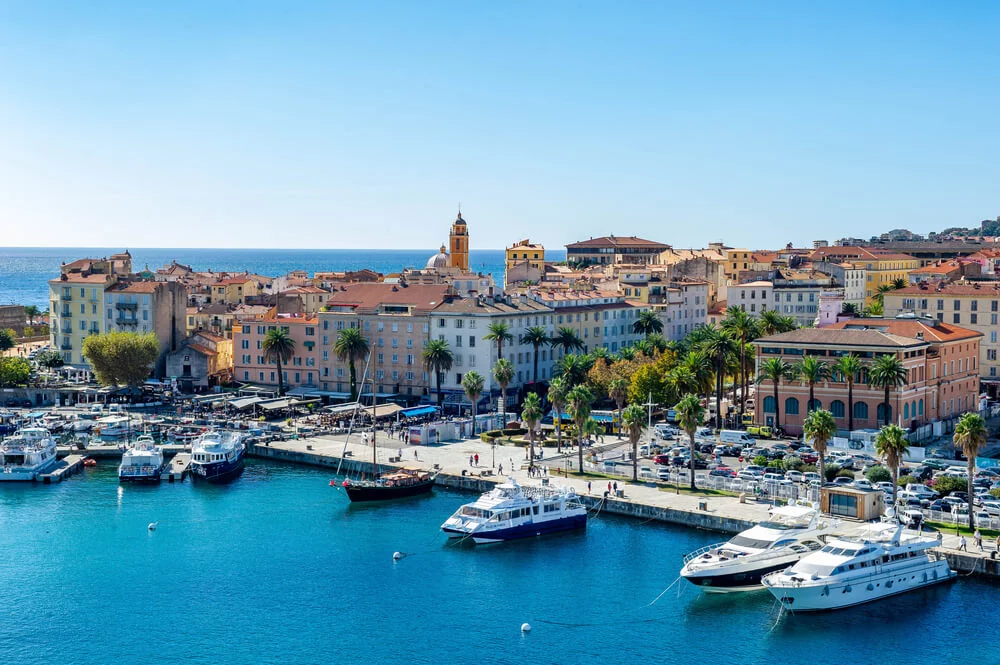 vue-panoramique-dajaccio-et-de-son-port Photographie de la ville d'Ajaccio en Corse, capturant le port animé entouré de maisons colorées et de palmiers sous un ciel bleu azur. Page Camping Corse bord de mer à Ajaccio
