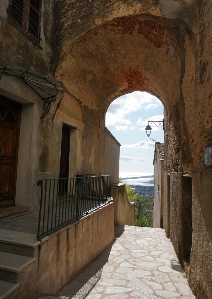 rue-pittoresque-a-bastia-vue-mer-sous-le-ciel-bleu Dans cette rue historique de Bastia, les anciennes bâtisses en pierre offrent une vue imprenable sur la mer Méditerranée, sous un ciel bleu azur.