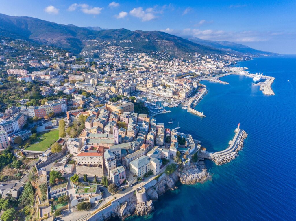 vue-aerienne-de-bastia-petite-perle-de-corse Vue aérienne de Bastia en Corse, mettant en valeur ses maisons colorées et son port animé sur fond de montagnes et de mer.