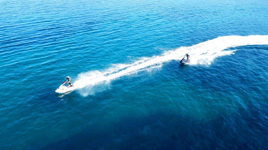 excursion-en-jet-ski-sur-une-mer-cristalline Deux personnes en jet ski traversent les eaux translucides d'une côte bleue, symbolisant l'adrénaline et la liberté de l'aventure nautique.
