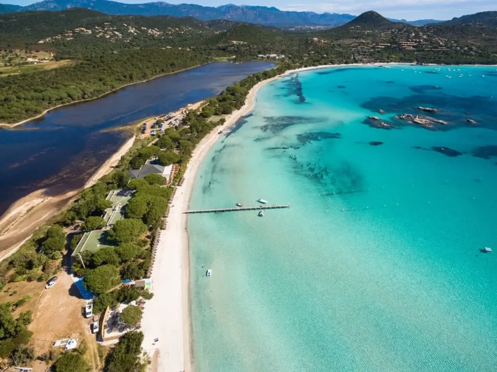 Photo de drone de Santa Giulia montrant la séparation entre l'étang et la mer turquoise, bordée par une forêt de pins.