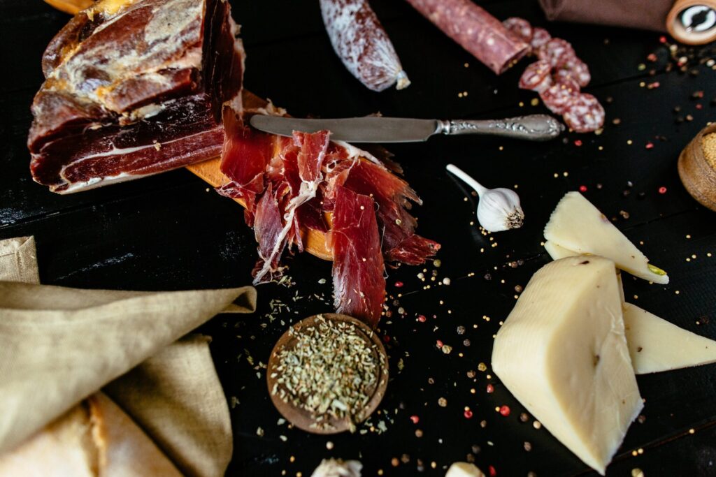 plateau-de-charcuterie-avec-jambon-fromage-et-epices Plateau de charcuterie alléchante avec jambon, fromage varié, épices colorées et gousses d'ail sur une table en bois sombre, idéal pour une dégustation conviviale.