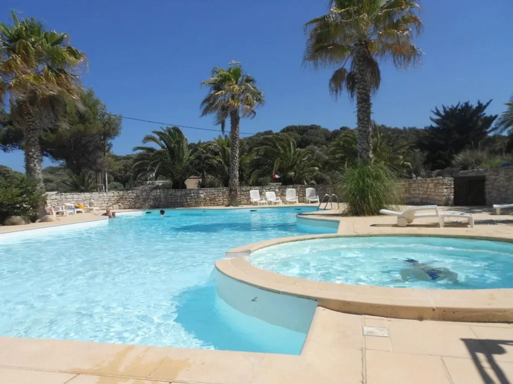detente-au-bord-de-la-piscine-a-bonifacio Sous le ciel bleu de Bonifacio, la piscine du camping Cavallo Morto offre un espace de détente idéal, entourée de palmiers et d'une eau cristalline, parfait pour des vacances estivales en famille.