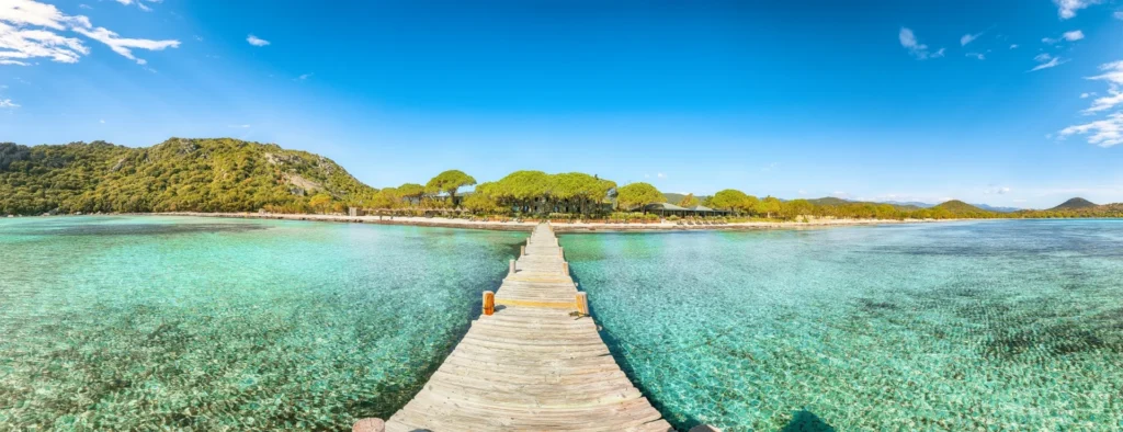 Plage de Santa Giulia Ponton en bois avançant sur les eaux transparentes de la plage de Santa Giulia, entourée de collines verdoyantes.