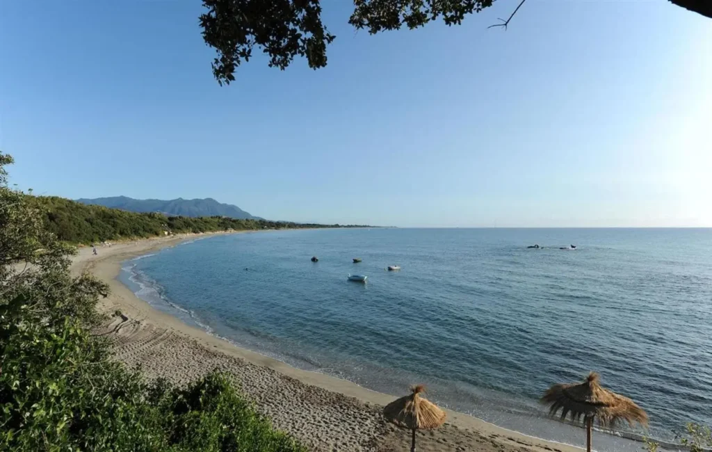 Plage en Corse au bord de mer avec mer calme et bateaux au mouillage, vue idéale pour un séjour en camping naturiste (naturisme).