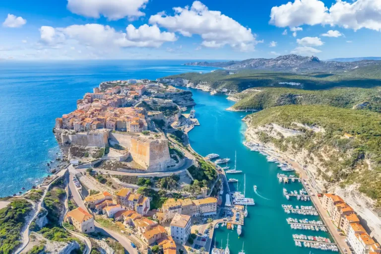 Vue aérienne spectaculaire de la citadelle de Bonifacio perchée sur ses falaises de calcaire blanc dominant la mer et le port de plaisance.
