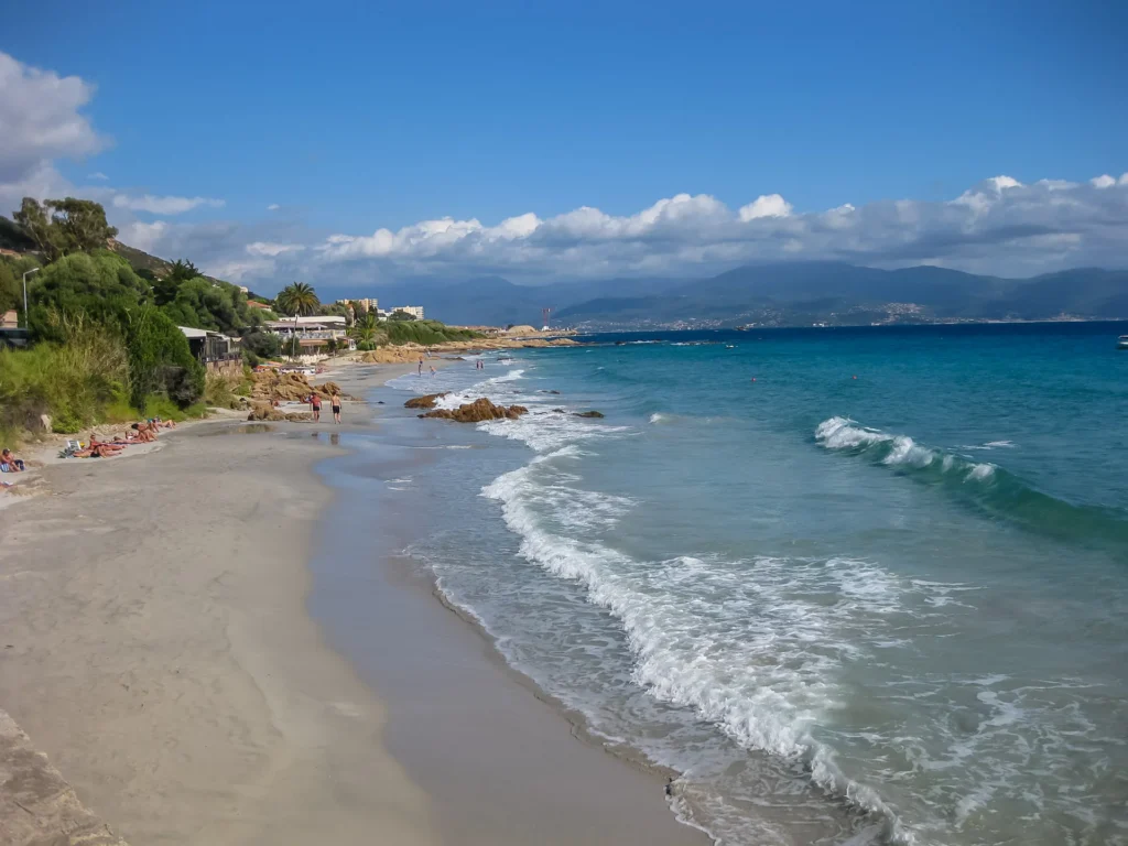 Plage de sable fin de Barbicaja à Ajaccio bordée par des eaux turquoise, située au pied du camping avec vue sur les montagnes corses.