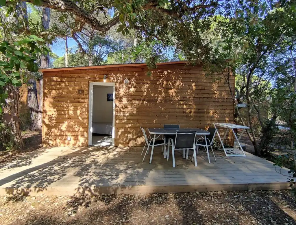Chalet éco-lodge en bois au Camping Villata avec terrasse privée et salon de jardin, niché sous l'ombre des pins parasols.