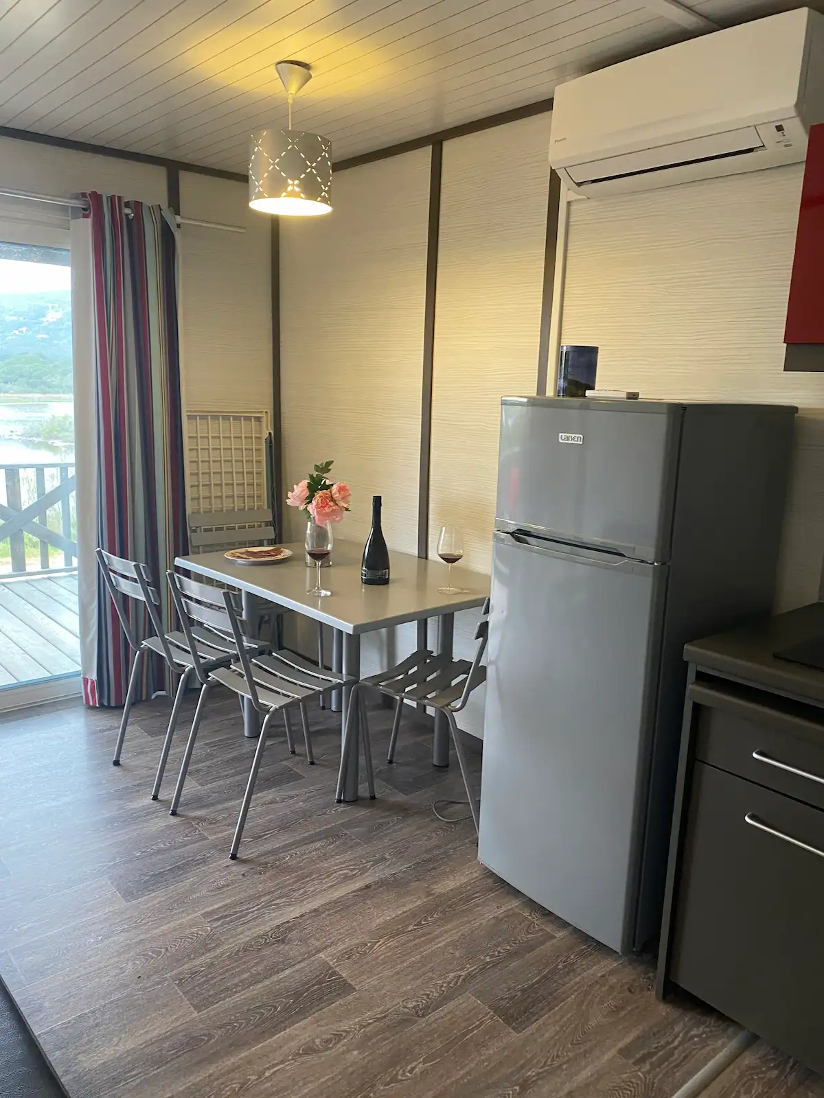 Coin repas lumineux d'un mobil-home au Camping Villata avec vue sur l'étang et cuisine équipée.