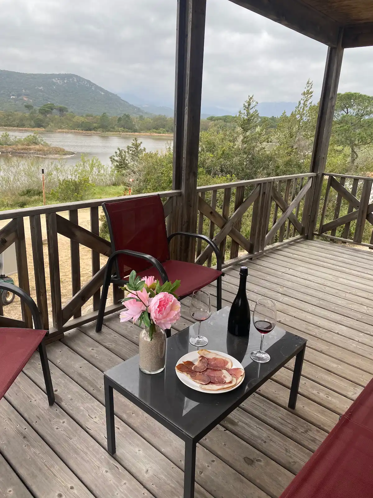 Plateau de charcuterie corse et vin servis sur la terrasse d'un chalet avec vue panoramique sur l'étang de Villata.