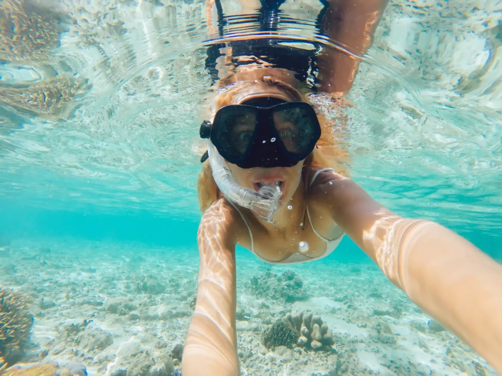 Femme pratiquant le snorkeling dans les eaux turquoise d'une plage en Corse, portant un masque et un tuba, vue sous-marine sur les fonds sableux.