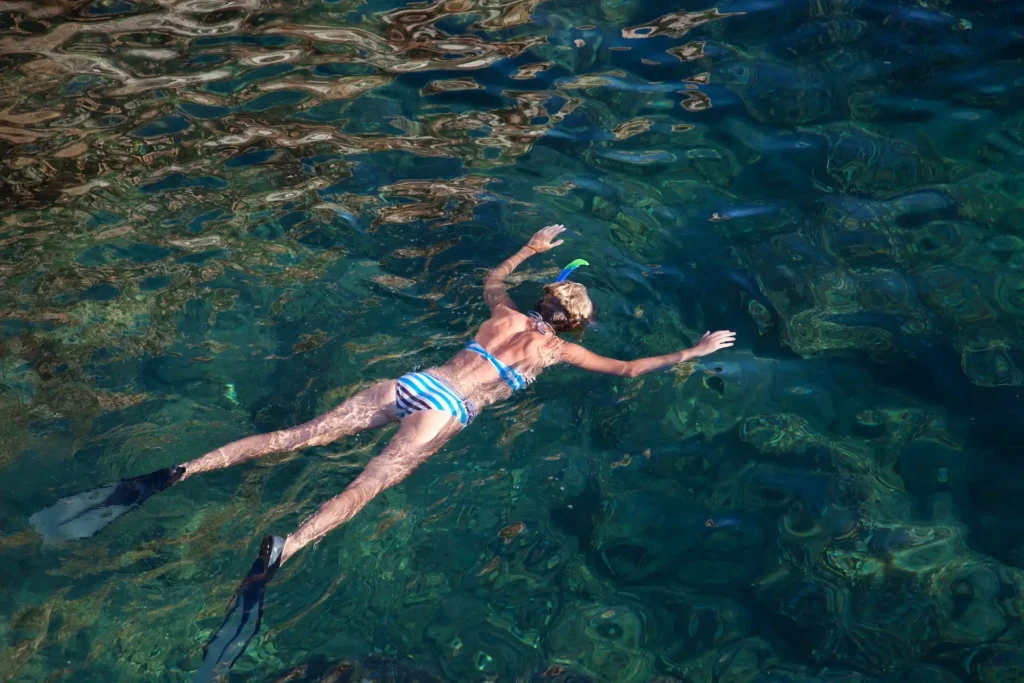 Plus beaux endroits pour plongée amateur snorkeling en Corse Vue aérienne d'une femme nageant en surface avec palmes, masque et tuba dans une crique rocheuse en Corse aux reflets vert émeraude.