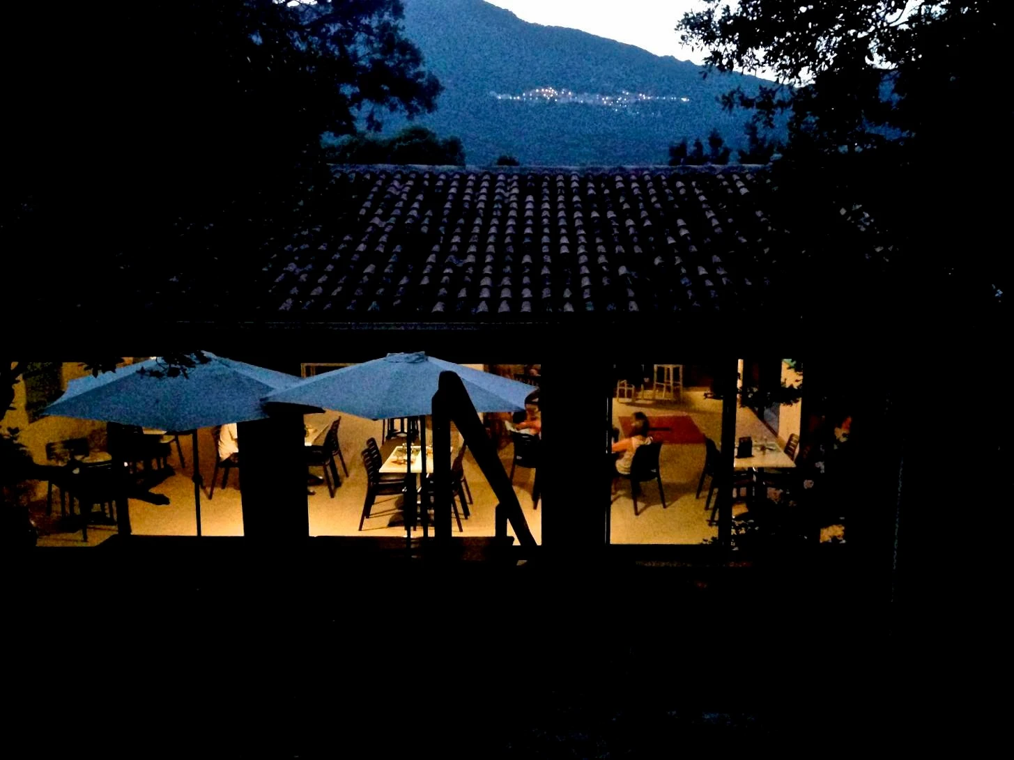 Terrasse du restaurant du Camping Milella illuminée en soirée avec vue panoramique sur les montagnes corses et les lumières d'un village au loin.
