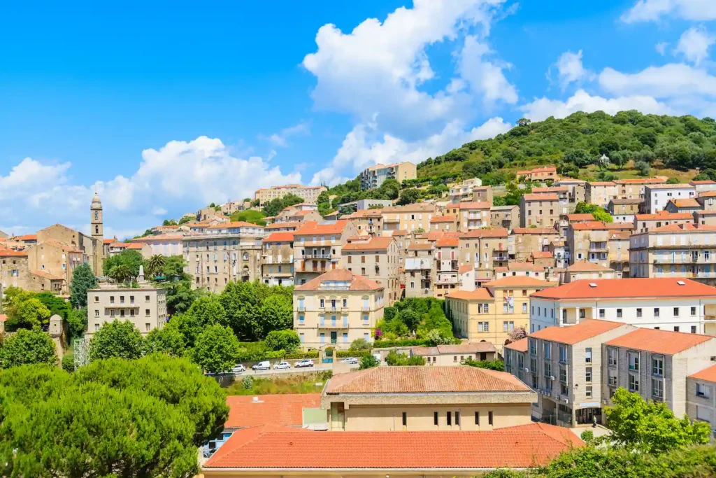 Vue du village de Sartène Valinco Vue panoramique sur du village traditionnel de Sartène en corse avec ses maisons en pierre aux toits de tuiles, niché au cœur d'une colline verdoyante sous un ciel bleu.