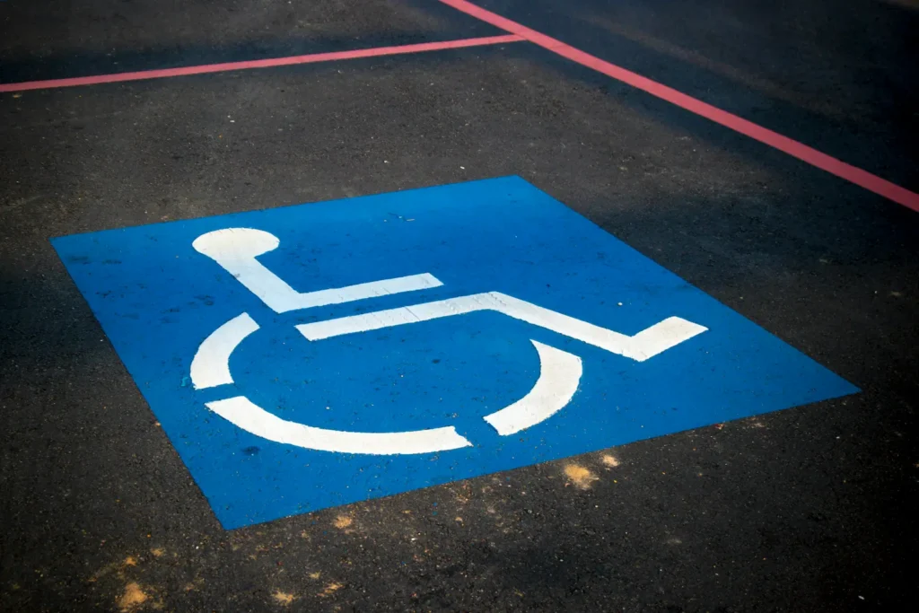 emplacement-hébergement-handicap-PMR-camping-corse-bord-de-mer Symbole international d'accessibilité représentant une personne en fauteuil roulant peint en blanc au centre d'un carré bleu sur le bitume d'une place de stationnement réservée.