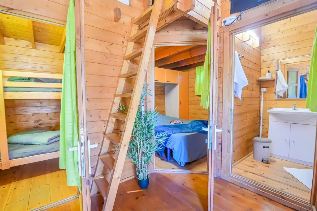chalet-pas-cher-grande-famille-corse Vue de l'intérieur d'un chalet en bois au camping montrant une chambre avec lits superposés, un espace parental et une salle de bain fonctionnelle.