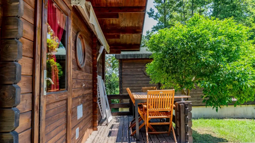 location-chalet-corse-en-camping Terrasse en bois meublée d'une table et de chaises en teck avec store banne, attenante à un chalet en bois en camping en Corse du Sud.